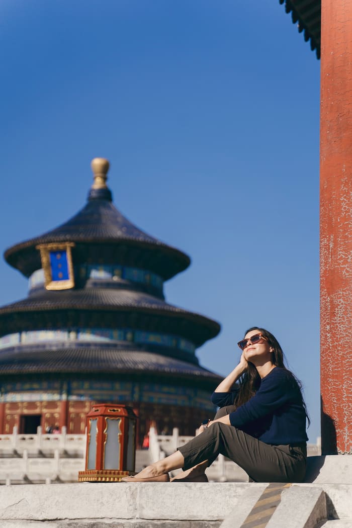 Mujer turista con lentes de sol sentada sobre el suelo disfrutando del sol de Beijing, gracias a los servicios de la agencia especializada en china